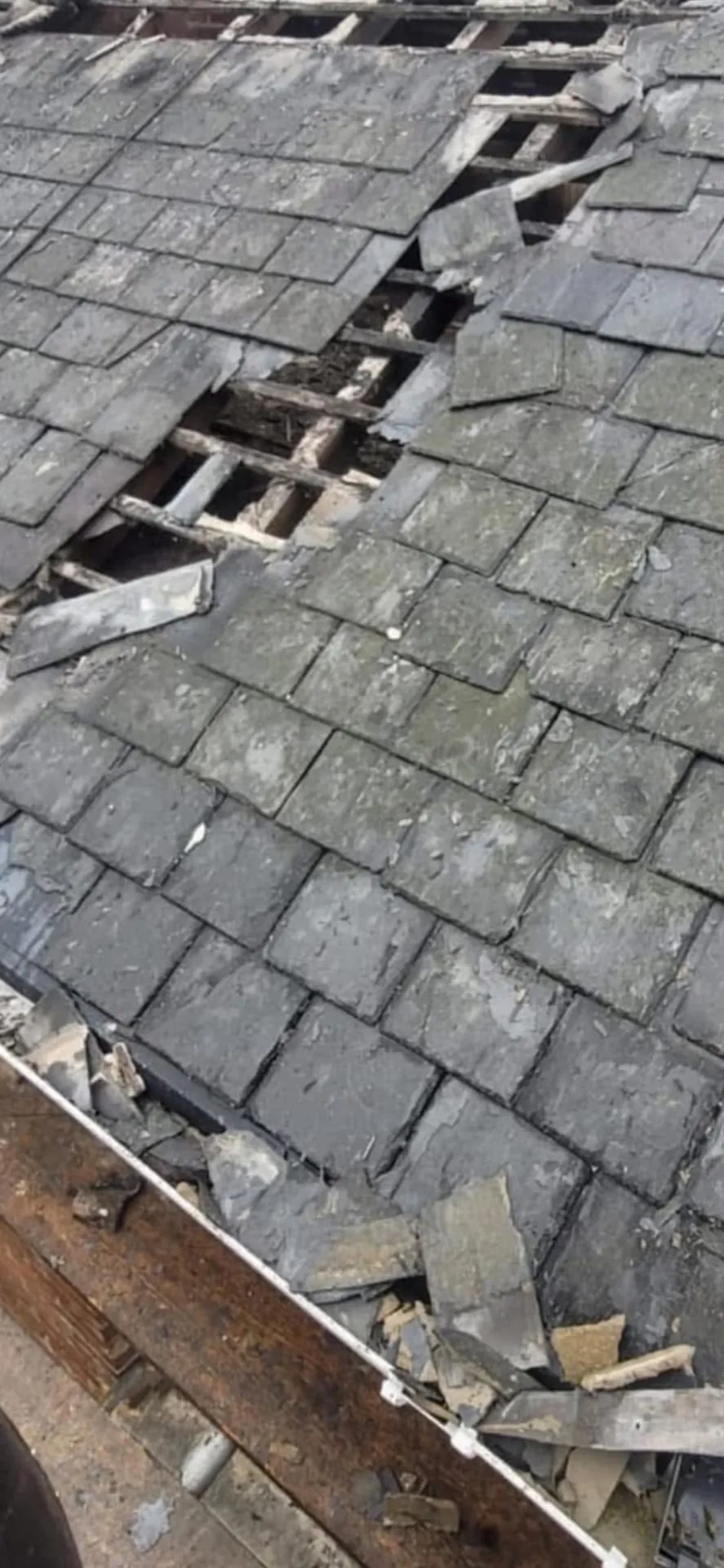Storm-damaged slate roof with missing slates and exposed battens before repair
